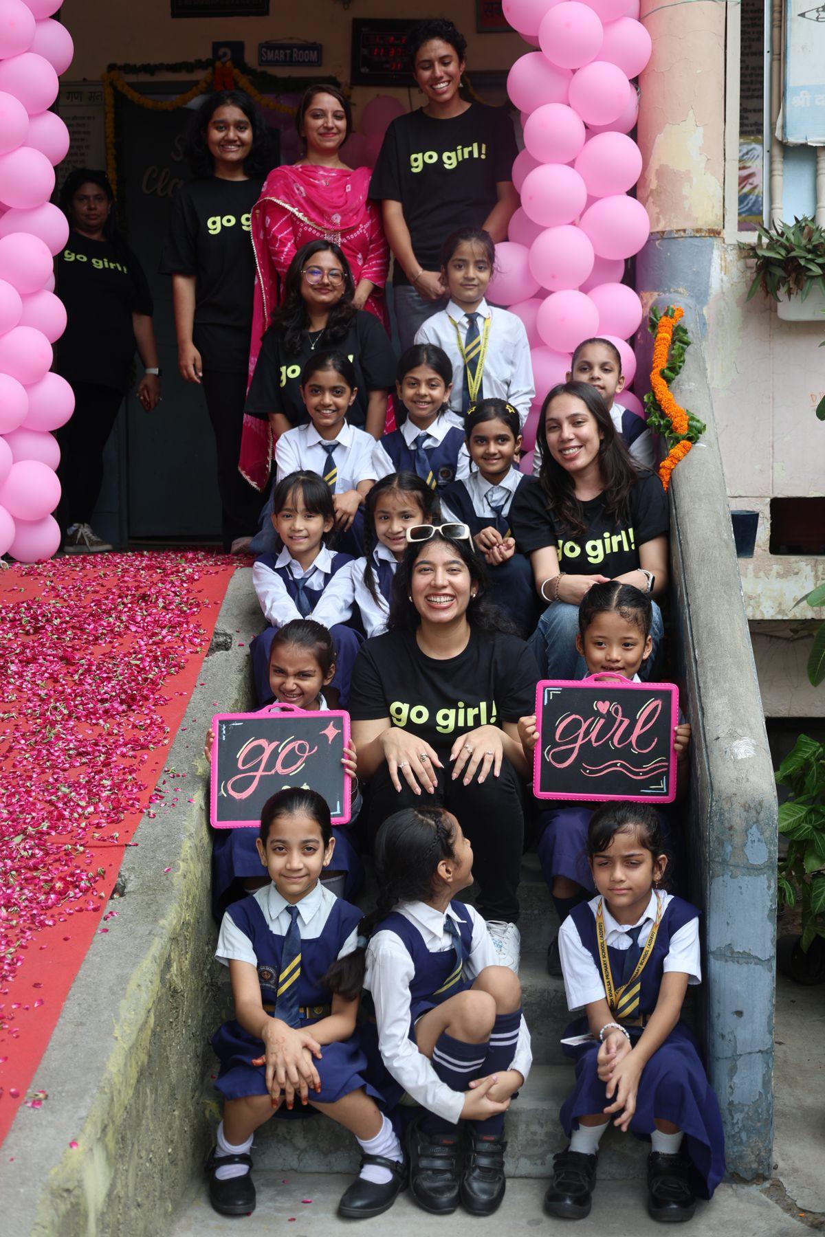 Go Girl volunteers and students on the school steps holding 'go' and 'girl' signs