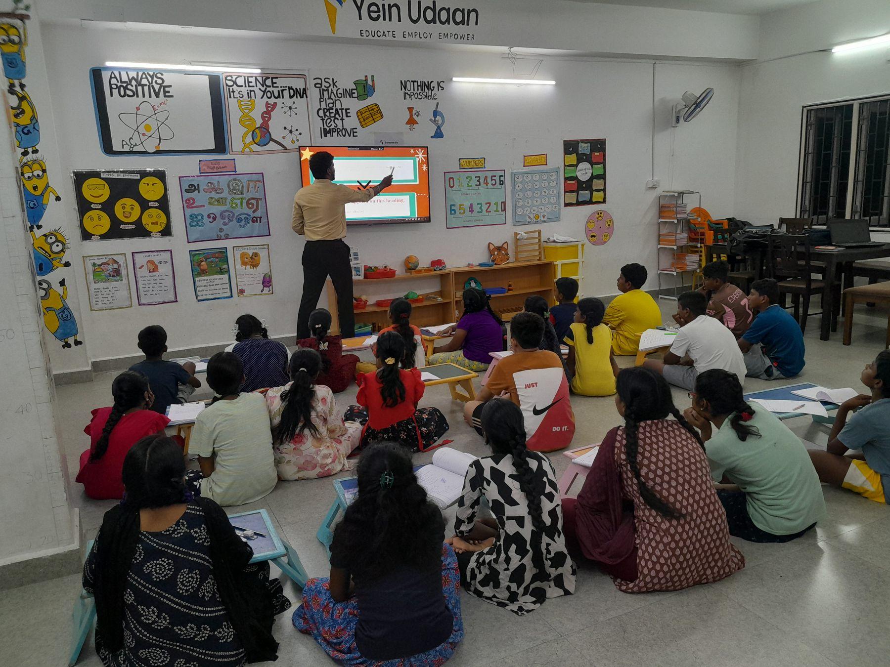 A tutor teaching a room of students at a digital board